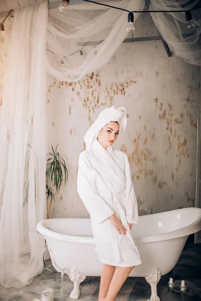 Gadis yang menarik mengenakan jubah mandi putih dan handuk di kepala di kamar mandi — Stok Foto