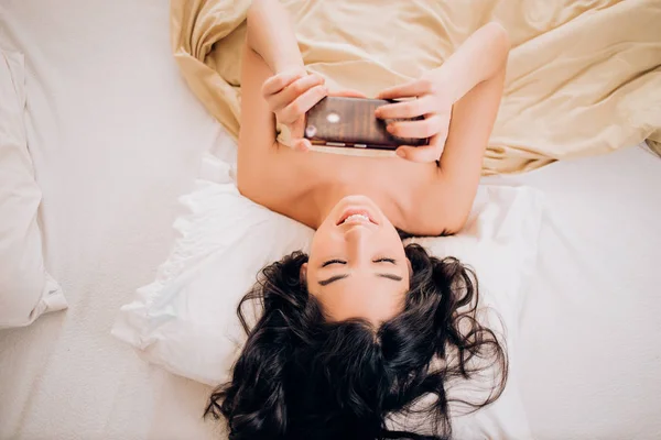Beautiful young smiling brunette woman using phone in her bedroom