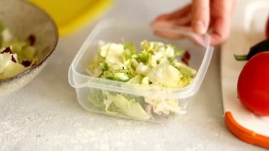 Woman hands lays out fresh delicious salad, cabbage leaves and arugula in a container. Healthy food, diet