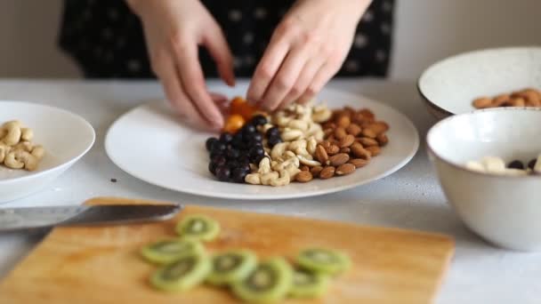 一个女人准备一个美味和健康早餐 把他的手腰果 奇异果和香蕉片在一个大的白色菜 — 图库视频影像
