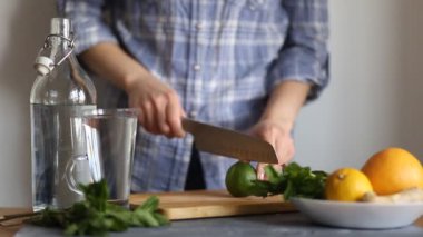 Mavi gömlekli bir kadın masanın mutfağında limon ve nane ferahlatıcı bir içecek hazırlar, bir bıçakla meyve keser, closeup. Yaz konsepti