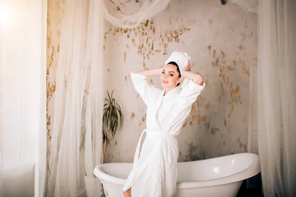 Aantrekkelijk meisje dragen witte badjas en handdoek op hoofd in de badkamer — Stockfoto