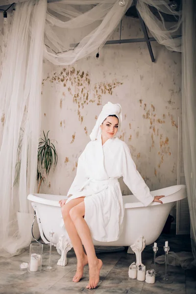 Attraktives Mädchen mit weißem Bademantel und Handtuch auf dem Kopf im Badezimmer — Stockfoto