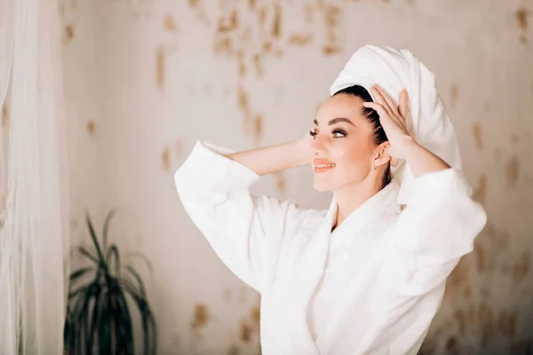 Attractive girl wearing white bathrobe and towel on head in bathroom — Stock Photo, Image