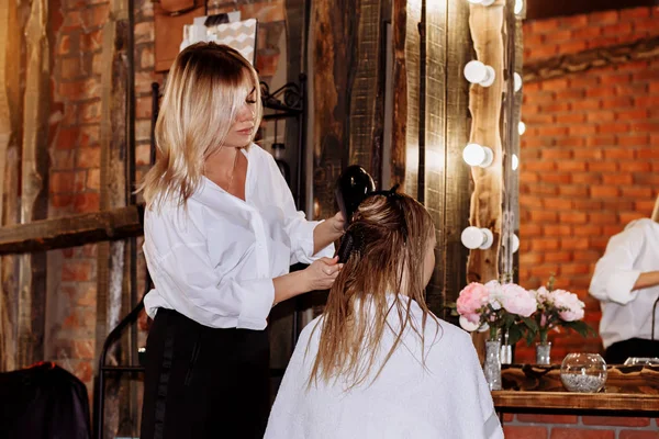 Primer plano de la mujer peluquera haciendo peinado al cliente con el pelo largo y rubio —  Fotos de Stock