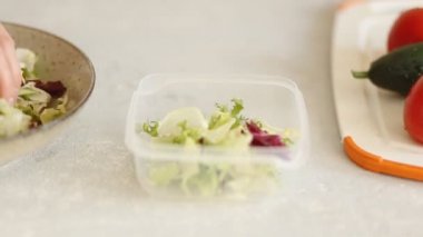 Woman hands lays out fresh delicious salad, cabbage leaves and arugula in a container. Healthy food, diet