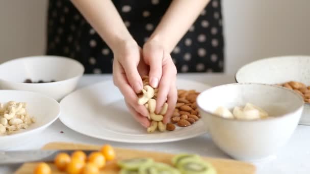 Žena připravuje lahodnou a zdravou snídani, položí si ruce na ořechy, mandle a borůvky ve velkém bílém talíři, v šatně