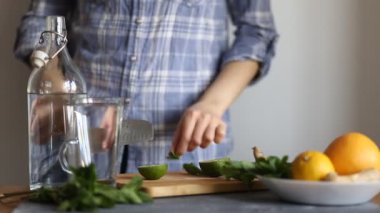 Mavi gömlekli bir kadın masanın mutfağında limon ve nane ferahlatıcı bir içecek hazırlar, bir bıçakla meyve keser, closeup. Yaz konsepti