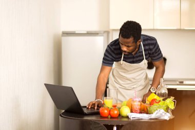 Evdeki mutfakta dizüstü bilgisayarda yemek tarifi arayan bir adam.