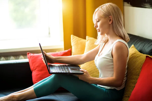 Jovem mulher usando laptop enquanto relaxa no sofá — Fotografia de Stock