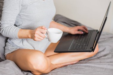 Yatakta bir fincan kahve içerken dizüstü bilgisayar kullanan pretty kadın