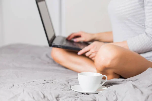 Красива жінка використовує ноутбук, маючи чашку кави на ліжку — стокове фото