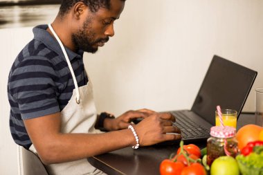 Evdeki mutfakta dizüstü bilgisayarda yemek tarifi arayan bir adam.
