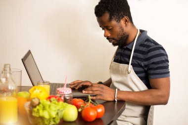 Evdeki mutfakta dizüstü bilgisayarda yemek tarifi arayan bir adam.