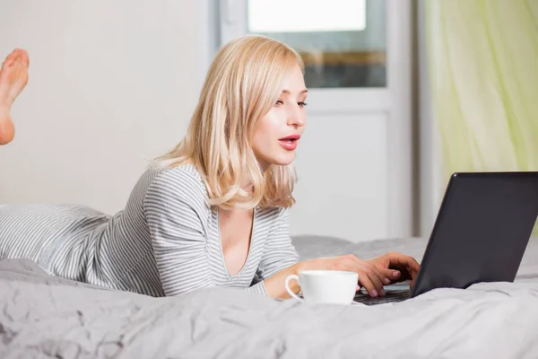 Όμορφη γυναίκα που χρησιμοποιεί φορητό υπολογιστή ενώ έχει ένα φλιτζάνι καφέ στο κρεβάτι — Φωτογραφία Αρχείου