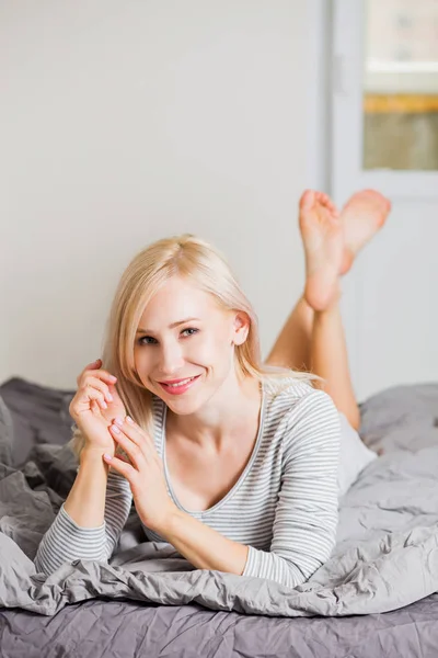 Positiv kvinna som ligger på sängen och ler till kameran hemma — Stockfoto