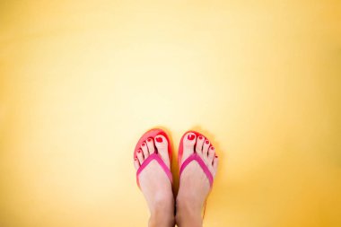 Kopya alanı ile sarı arka planda pembe parmak arası terlik giyen kadın bacakları