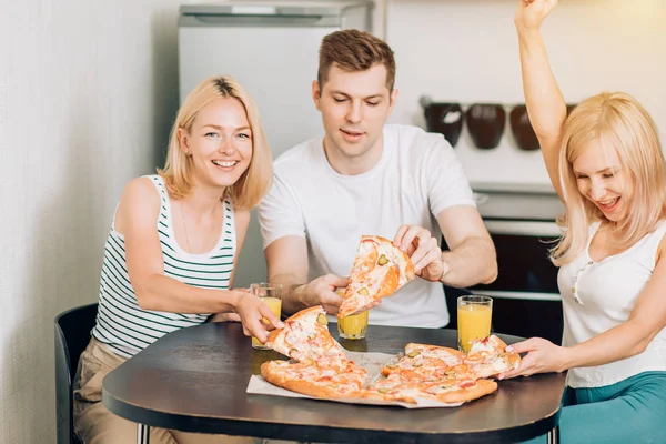 Young friends eating pizza in kitchen and smiling