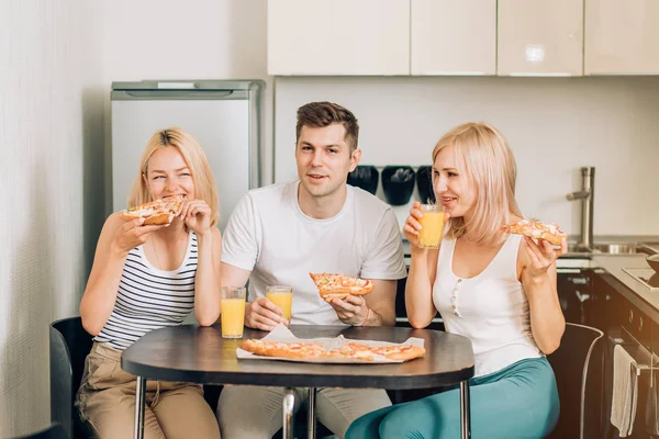 Jovens amigos comendo pizza na cozinha e sorrindo — Fotografia de Stock