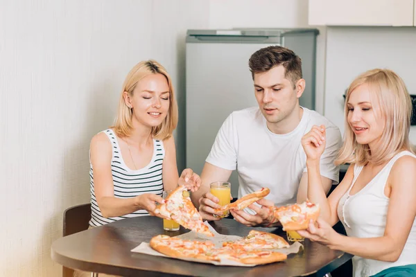 Jovens amigos comendo pizza na cozinha e sorrindo — Fotografia de Stock