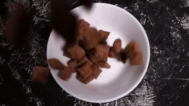 Closeup Flocos Chocolate Almofadas Caindo Uma Placa Branca Fundo Preto — Vídeo de Stock
