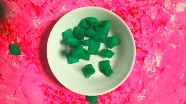 ピンクの背景 トップビュー上の白いプレートに落ちる緑のフレークの抽象的なスローモーションビデオ シリアル キッチンコンセプト — ストック動画