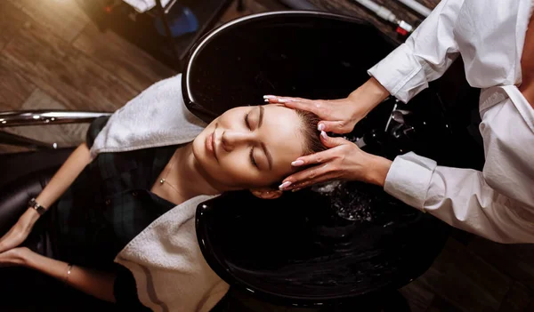 Underbar söt ung kvinna huvudmassage njuter samtidigt professionell frisör tillämpa schampo håret. Närbild på frisörsalong händerna tvätta hår till klienten. — Stockfoto