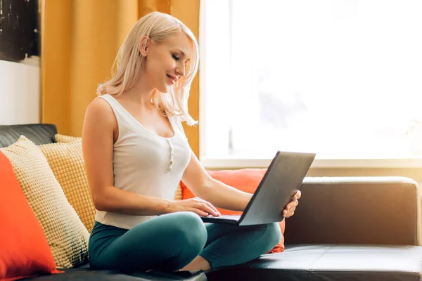 Молода жінка використовує ноутбук, розслабляючись на дивані — стокове фото
