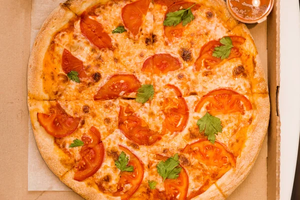 Dostawa pysznych świeżych pizzy w domu. Margarita z pomidorami, serem i sosem w pudełku na stole — Zdjęcie stockowe