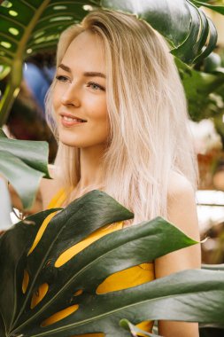 Yeşil tropikal bitkilerin arasında duran güzel görünümlü sarışın kadının dikey görüntüsü. Yağmur ormanlarında poz veren doğal güzelliği olan çekici bir kadın. Güzellik, cilt bakımı.
