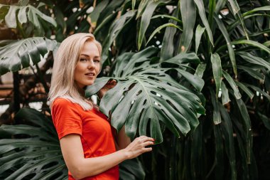 Profil portresi. Sarışın, beyaz, güzel bir kızın tropikal ormanda canavar yapraklarının önünde poz vermesi. Sağlıklı ciltli çekici bir model. Saflık, sağlık ve cilt bakımı.