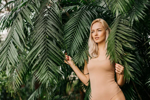 具有自然的裸体妆容 完美的皮肤 金发的快乐女士的画像 美丽的女人躲在棕榈叶后往下看 化妆品 — 图库照片