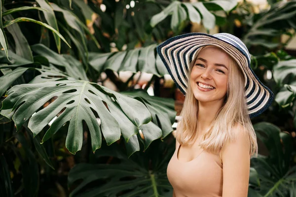 一个有着金发碧眼 头戴帽子 面带微笑 享受阳光 在热带度假胜地放松的快乐迷人的高加索年轻女子的垂直特写 夏季概念 — 图库照片