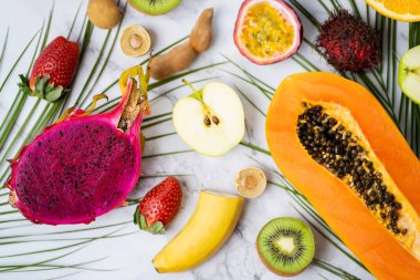 Masada dilimlenmiş egzotik taze meyveler. Beyaz arka planda çeşitli sulu tropikal yaz mevsimlik meyveleri ve tropik yapraklar. Seçici odaklanma. Dikey çekim.