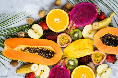 Farklı dilimlenmiş egzotik meyveler ve masada tropikal yapraklar. Üst Manzara. Dikey çekim. Sağlıklı yaşam tarzı, yemek, diyet, tatil, yaz mevsimsel meyve kavramı.