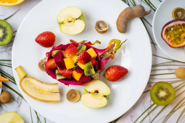 Set of exotic ripe juicy seasonal tropical fruits spread out on plate and on table. Top view of sliced fruits and tropical leaves. Flat lay summer composition.