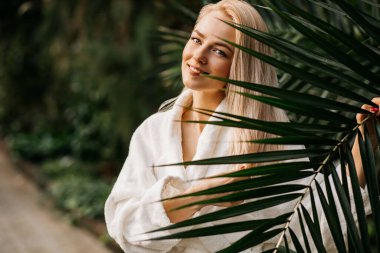 Yakından bakınca, egzotik bir ormanın arka planında beyaz önlüklü genç bir Spa kadınının güzel bir portresi görülüyor. Spa, tedavi, doğal kozmetik, cilt bakımı, kozmetoloji konsepti.