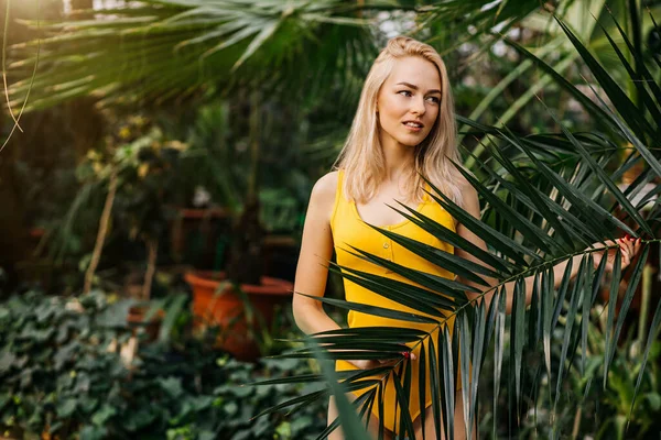 温和的女领事 金发碧眼 身材苗条 身穿黄色泳衣 日落时在热带植物的背景下摆姿势 夏天的概念 — 图库照片