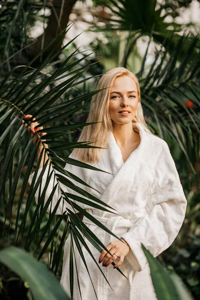 快乐可爱快乐的女模穿着白色浴衣站在棕榈叶后 面带微笑 天然化妆品 美容等概念 — 图库照片