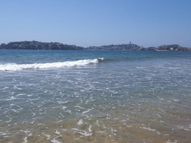 Meksika 'daki ACAPULCO şehrinin koyundaki ünlü kumlu plaj ve Pasifik Okyanusu manzaralarının beyaz dalgaları ve 2018' de açık mavi gökyüzü sıcak kış günü, Kuzey Amerika, Mart ayında.