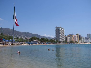 ACAPULCO, MEXICO NORTH AMERİKA Mart 2018 'de: Lüks oteller binaları ve Meksika bayrağı ile Meksika körfezinde kumsal panoraması, ılık, güneşli kış gününde açık mavi gökyüzü.