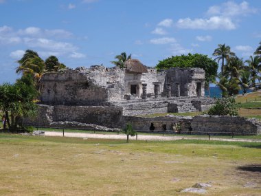Meksika 'nın Quintana Roo şehrinde bulunan Tulum kentindeki Maya tapınağının taşlı harabeleri ile şehir manzarası çimenli tarlalarda ve 2018' in ılık kış gününde bulutlu mavi gökyüzü..