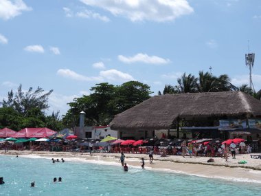 CANCUN, MEXICO NORTH AMERİKA Mart 2018: Şemsiyeler altında güneş banyosu yerleri, tropikal kumlu kaplumbağa plajlarında palmiye ağaçları Quintana Roo şehrinde turistler ve ılık güneşli kış gününde açık mavi gökyüzü.
