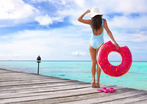 ピンクのドーナツのようなインナー チューブでポーズ ブルー ストライプ水着で若いブルネットの女性 — ストック写真