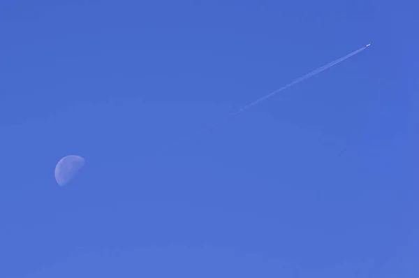 De maan en het pad van het vliegtuig tegen de blauwe hemel. — Stockfoto