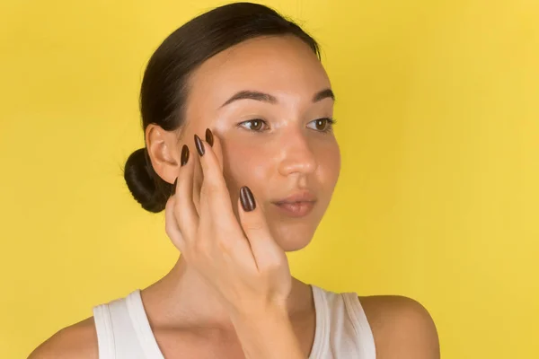 Menina bonita com pele perfeita tocando o rosto. Fundo amarelo — Fotografia de Stock