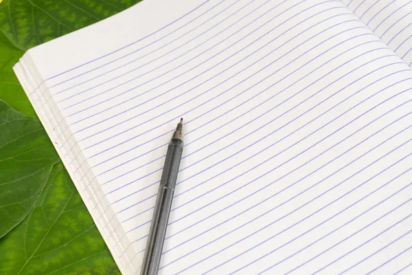 Kırtasiye seti. Parlak yeşil yaprakların arka planında boş bir defter ve kalem. Boşluğu kopyala
