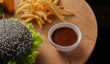 Patates ve sosu bir ahşap zemin üzerine siyah burger