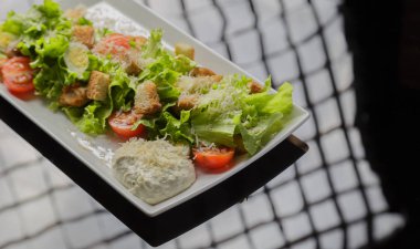 Sezar salatası beyaz bir tabak ve cam arka plan