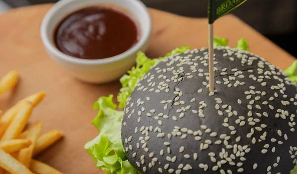 Schwarzer Burger auf Holzgrund mit Kartoffeln und Soße — Stockfoto